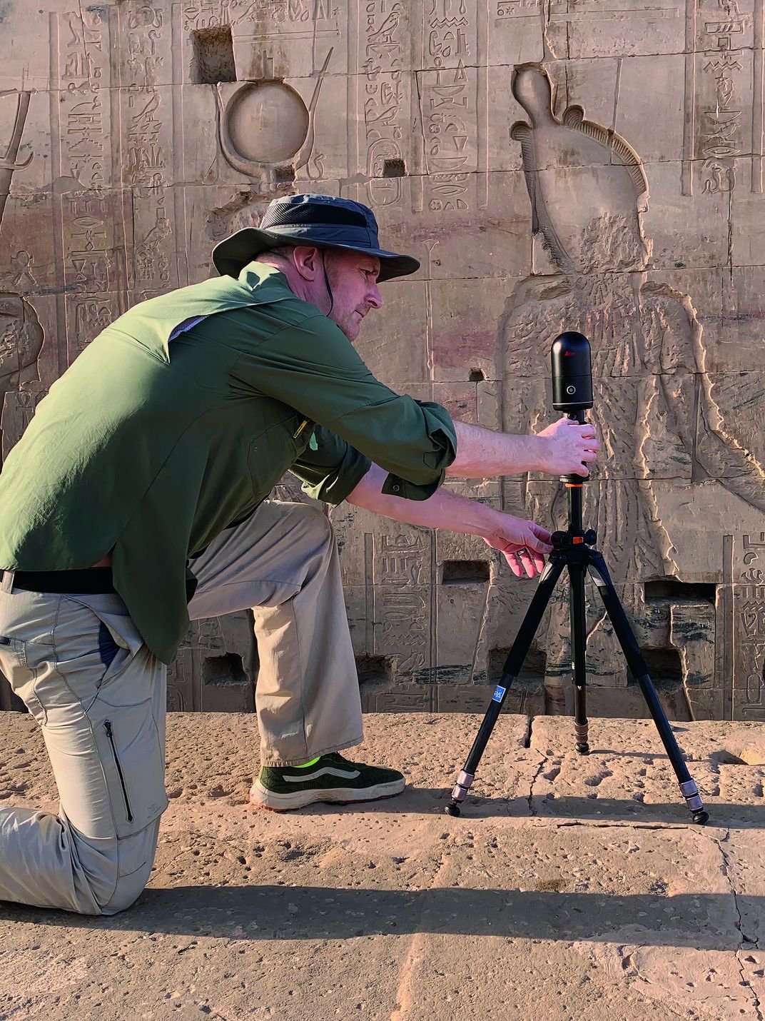 a man using a camera on tripod taking photos of ancient graffiti